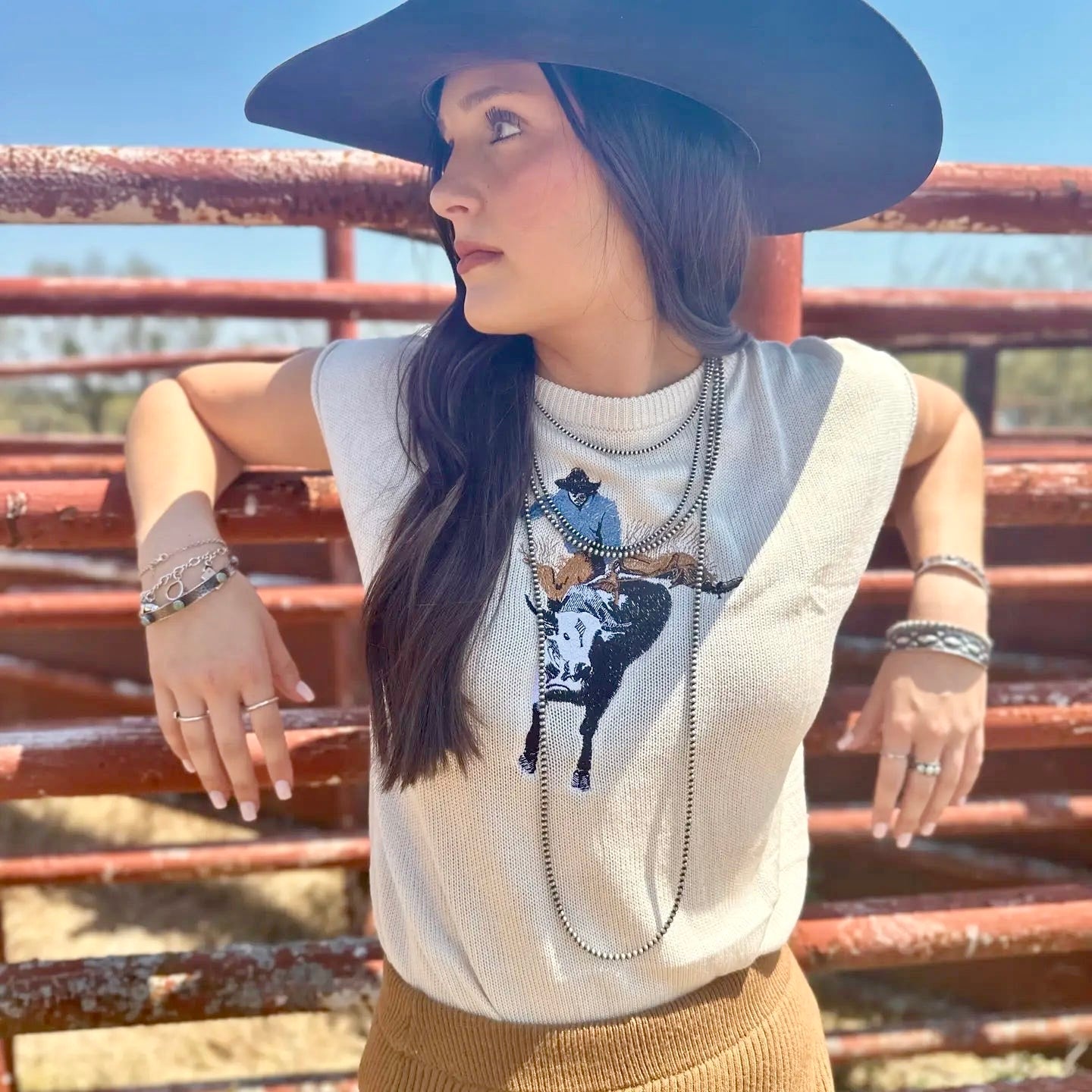 Woman wearing a sleeveless top with a graphic design in front of a rusted metal fence.