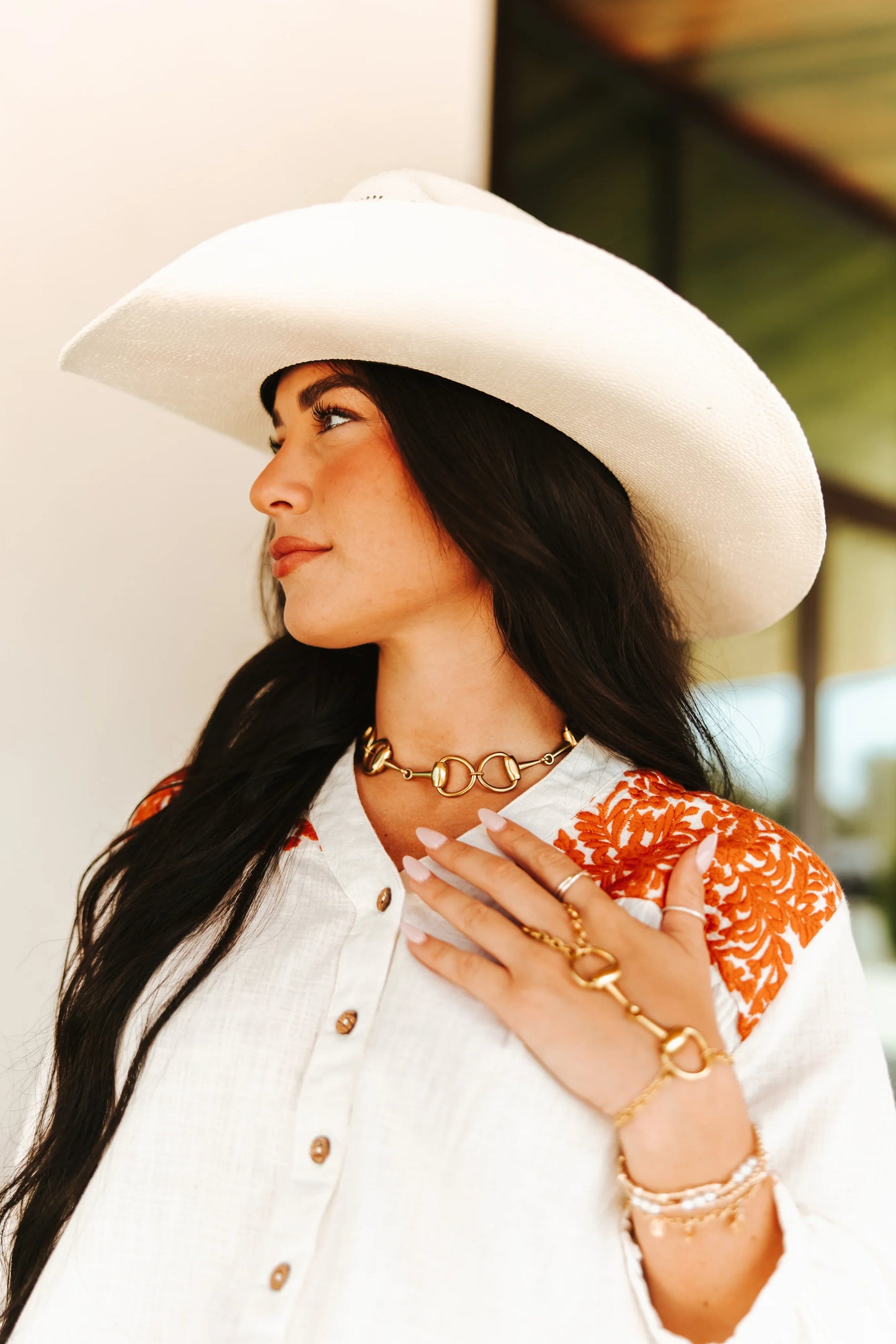 Woman wearing a white cowboy hat and gold jewelry outdoors