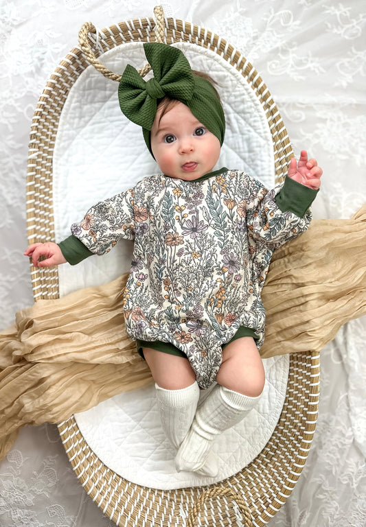 Baby in a floral onesie and green headband lying on a textured surface