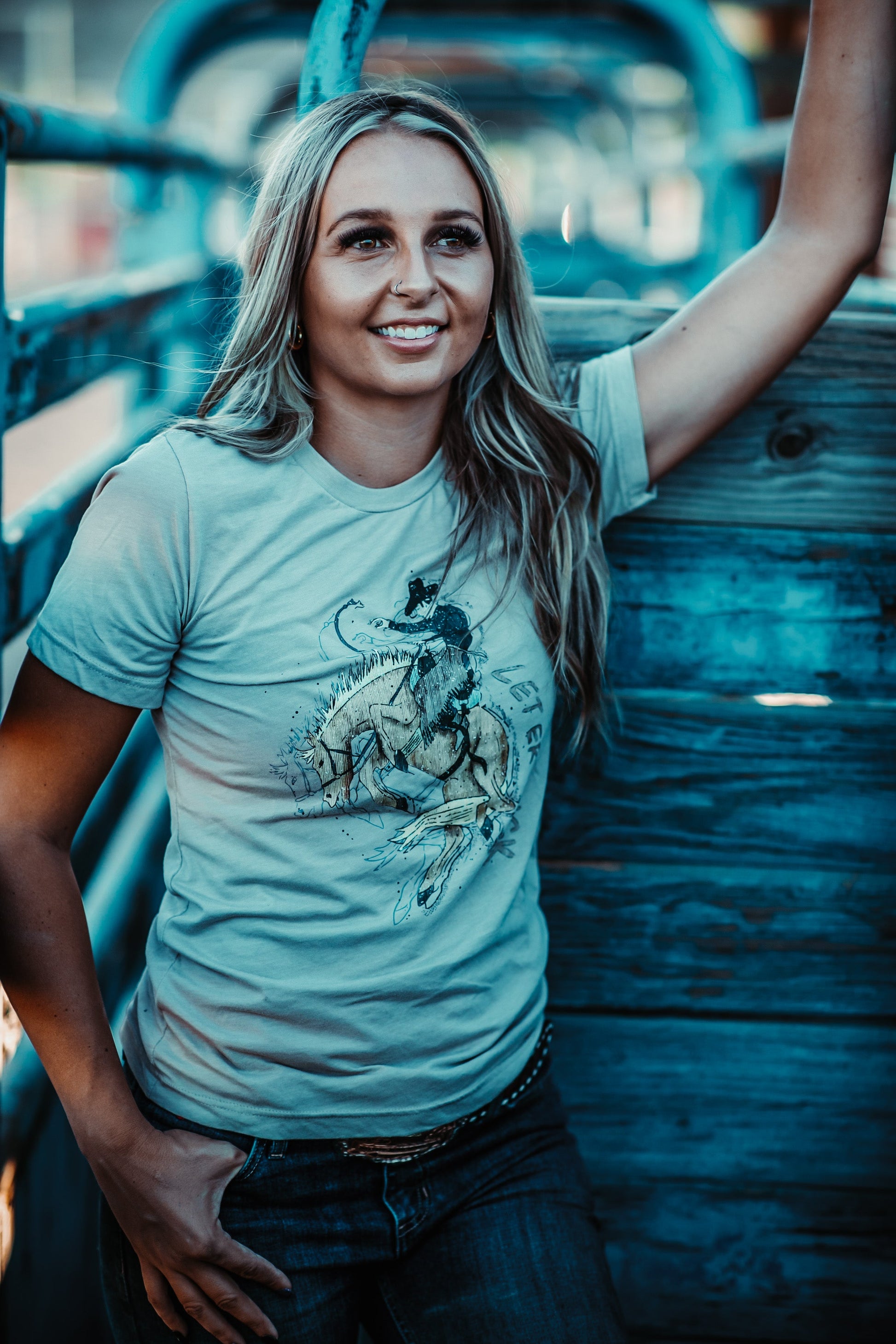 Woman wearing a light blue t-shirt with a graphic design, standing against a wooden background.
