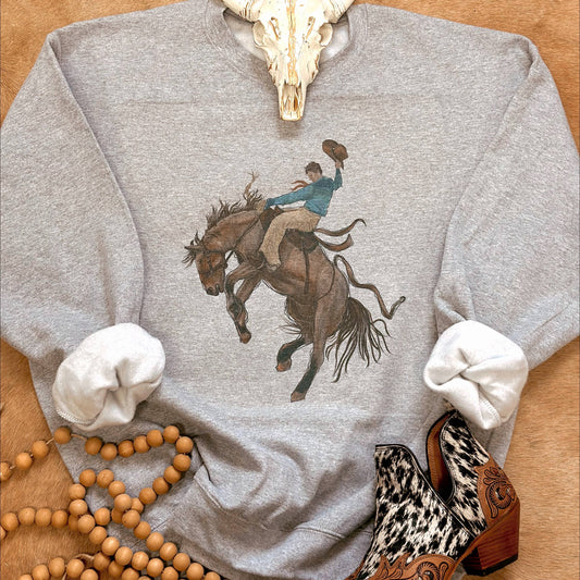 Gray sweatshirt with a graphic of a person riding a horse, surrounded by decorative items on a wooden surface.