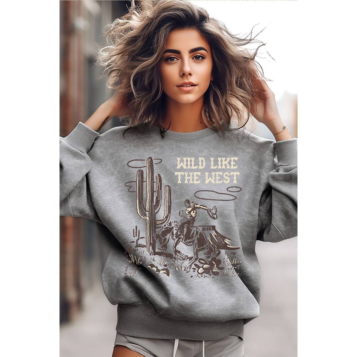 Woman wearing a gray sweatshirt with 'Wild Like The West' text and cactus design.